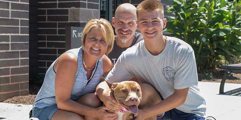 a family of three smiling outside the shelter with their newly adopted dog