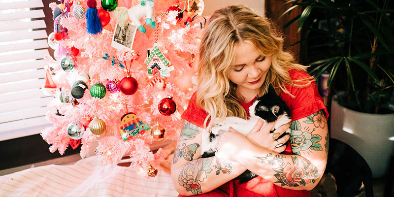 A LifeLine adopter is in her home holding a precious kitten in front of a Christmas tree